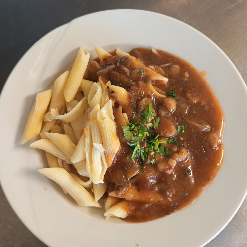 Ein weißer Teller mit Pasta und Pilzsauce, mit frischen Kräutern garniert.