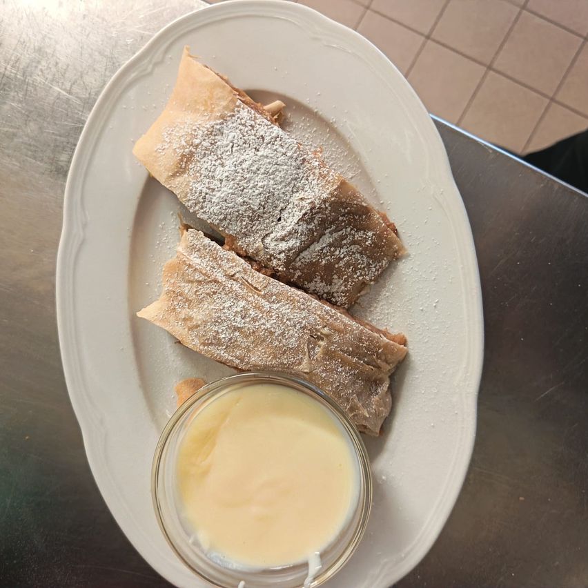 Ein Teller mit zwei gerollten Desserts, bestreut mit Puderzucker, begleitet von einer kleinen Schüssel Sahne.