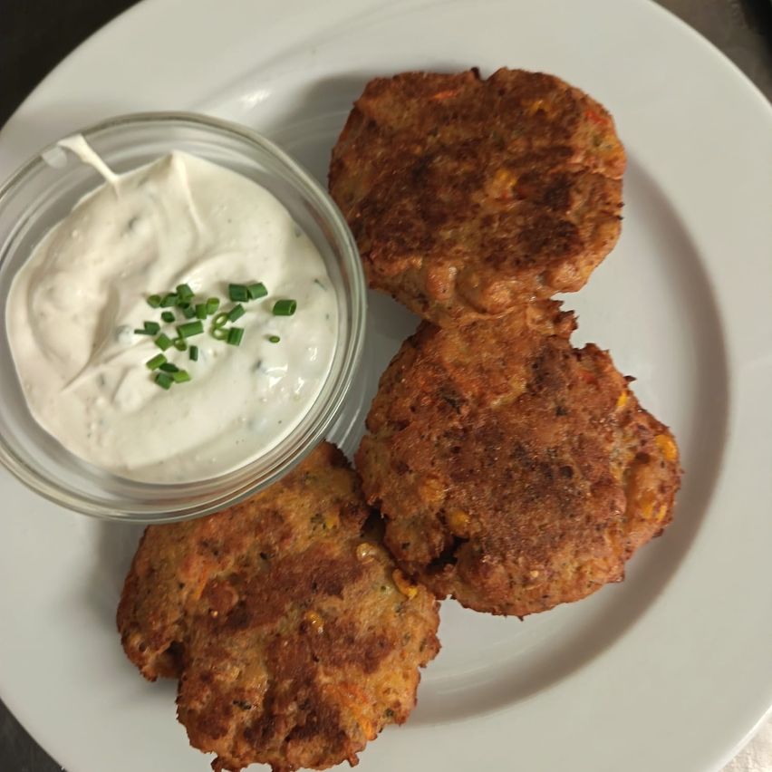 Three golden-brown patties with a crispy exterior and a creamy dip with green garnish on a white plate.