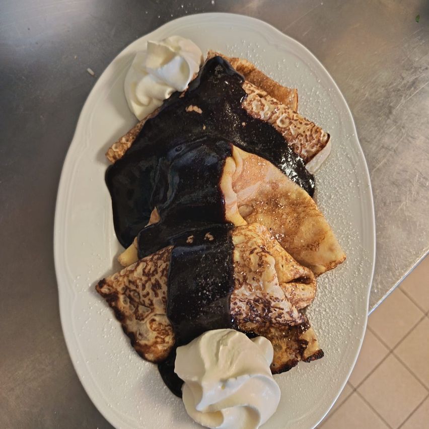 A plate of chocolate crepes with whipped cream and chocolate sauce. The crepes are golden brown and crispy on the edges.