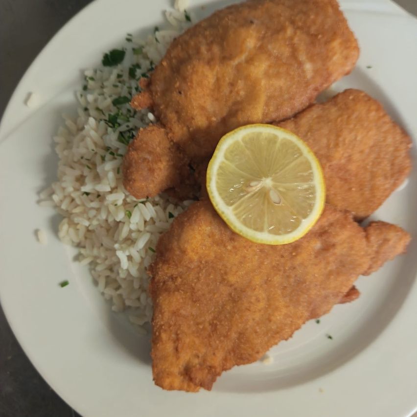 A white plate with fried fish pieces and rice. A lemon slice rests atop the fish.
