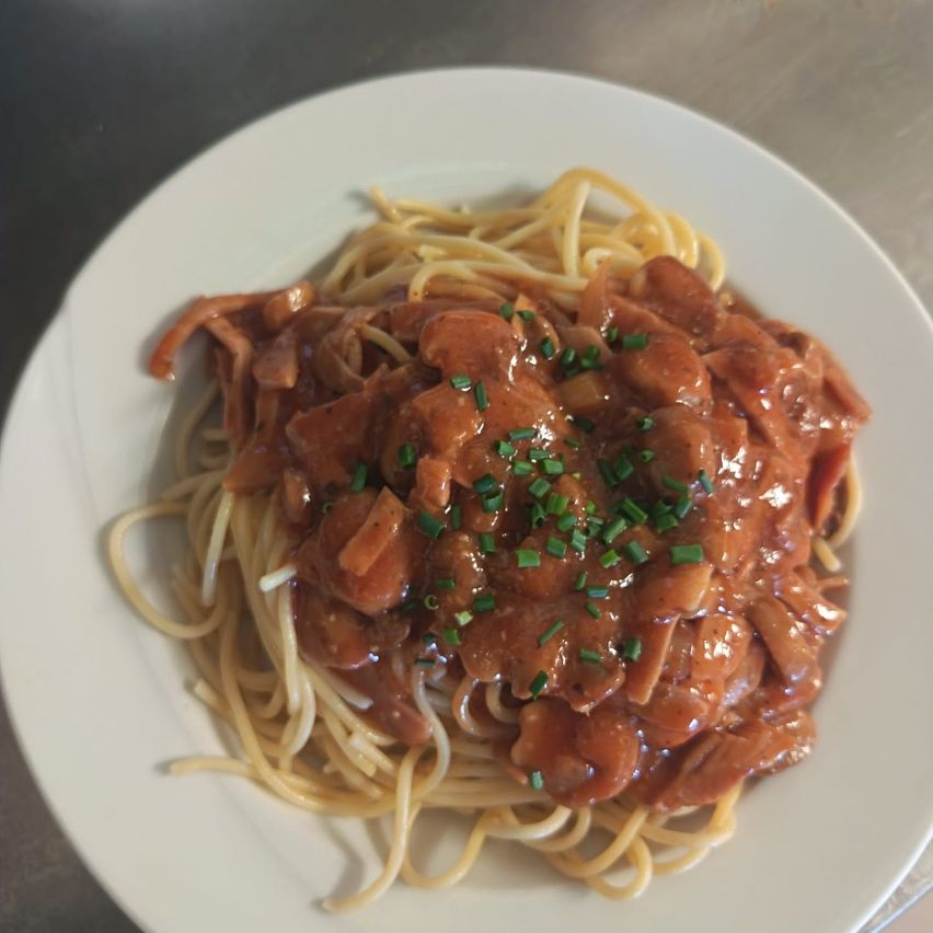 A plate of spaghetti with a rich, brown mushroom sauce and green herbs sprinkled on top.