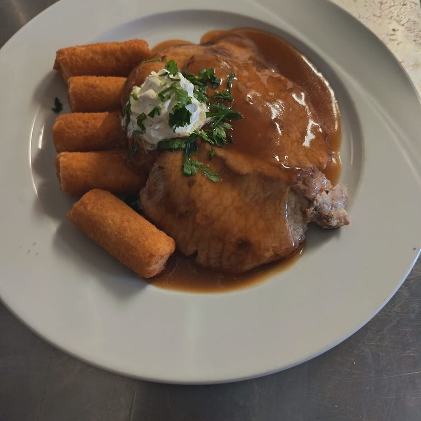 A plate with a sliced meat dish covered in gravy, topped with sour cream and parsley, accompanied by fried potato sticks.