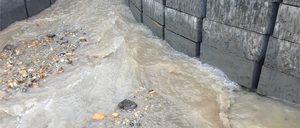 Eine Betonmauer leitet Wasser durch einen engen Spalt, was zu schnellem Fluss und Ansammlung von Trümmern führt.
