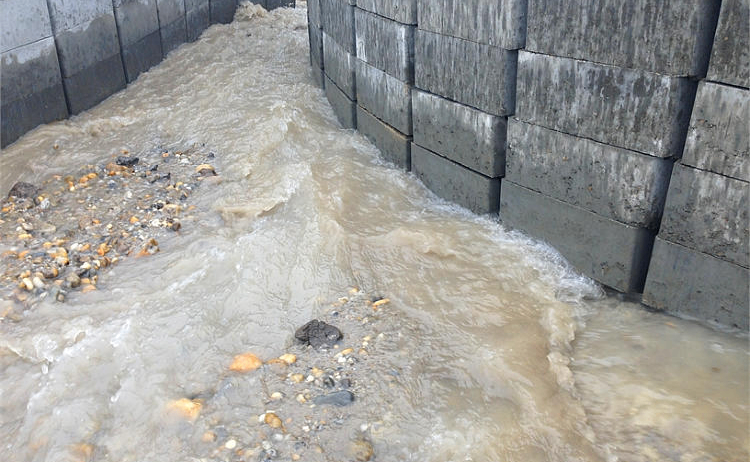 Eine Betonmauer leitet Wasser durch einen engen Spalt, was zu schnellem Fluss und Ansammlung von Trümmern führt.