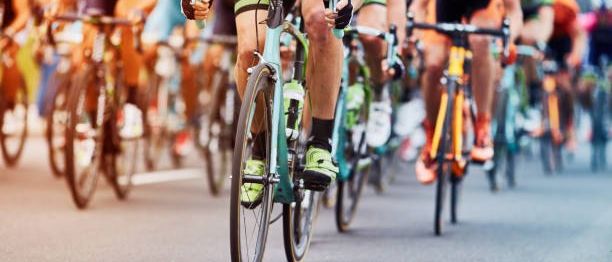 Eine Gruppe von Radfahrern in Radbekleidung, die bei einem Rennen auf einer asphaltierten Straße unterwegs sind.
