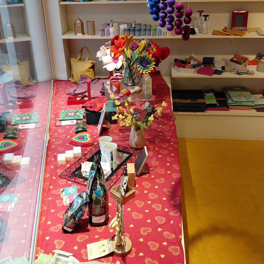 A store interior featuring a red table with a vase of flowers, various items, and shelves with products.