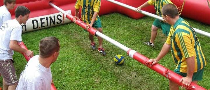 Eine Gruppe von Männern spielt ein Spiel mit aufblasbarem Fußball auf einem Rasenfeld.