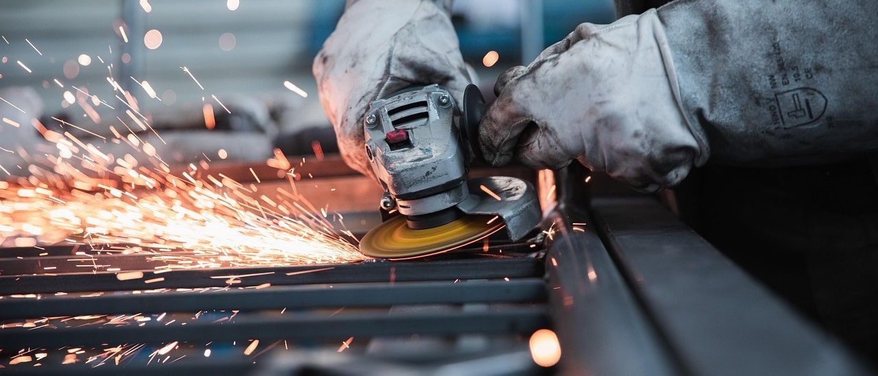 Eine Person in Schutzhandschuhen benutzt einen Winkelschleifer zum Schneiden von Metall und erzeugt Funken. Die Person steht auf einer Metalloberfläche.