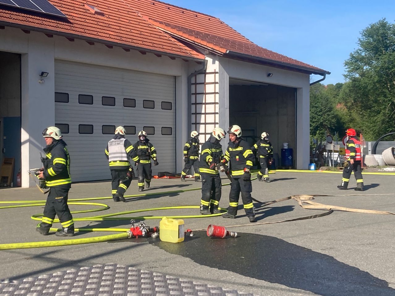 Feuerwehrleute in Schutzkleidung stehen vor einer Feuerwache, mit Feuerwehrschläuchen und Ausrüstung um sie herum verstreut.