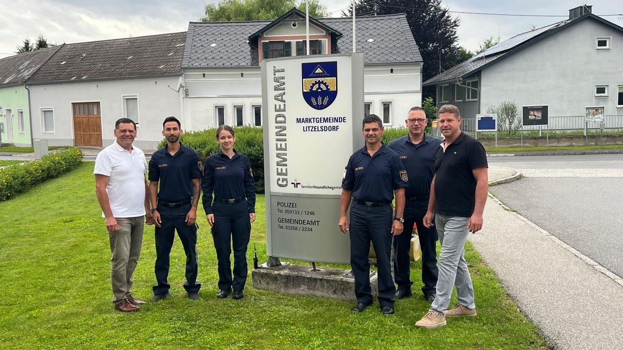 Fünf Männer und eine Frau in Uniform stehen vor einem Schild für Gemeindeamt, einem lokalen Regierungsbüro in Litzelsdorf. Dahinter ist ein Grasbereich mit einem Haus.