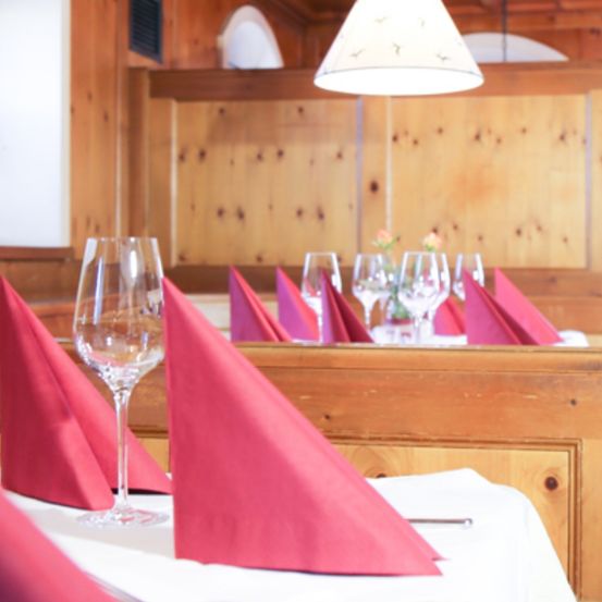 A dining table set with red napkins, wine glasses, and a lamp. The wooden walls and ceiling reflect light from the lamp.