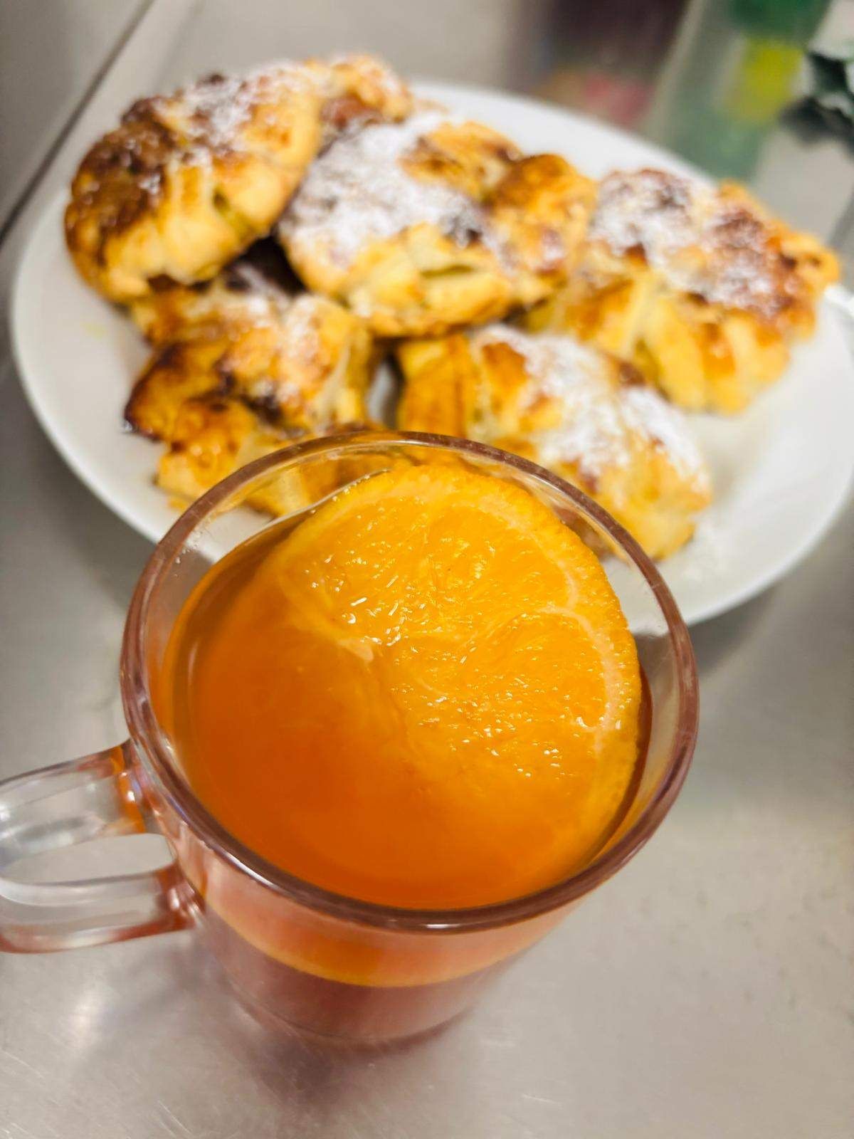 A plate of pastries, dusted with powdered sugar, is accompanied by a glass of orange juice with a slice of orange inside.