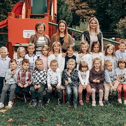 Eine Gruppenaufnahme von Kindern und Lehrern auf einem Spielplatz, die für ein Foto lächeln.