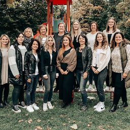 Eine Gruppe von Frauen posiert für ein Foto im Park, mit einer Spielstruktur im Hintergrund.