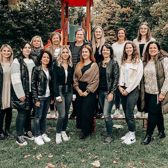 Eine Gruppe von Frauen posiert für ein Foto im Park, mit einer Spielstruktur im Hintergrund.