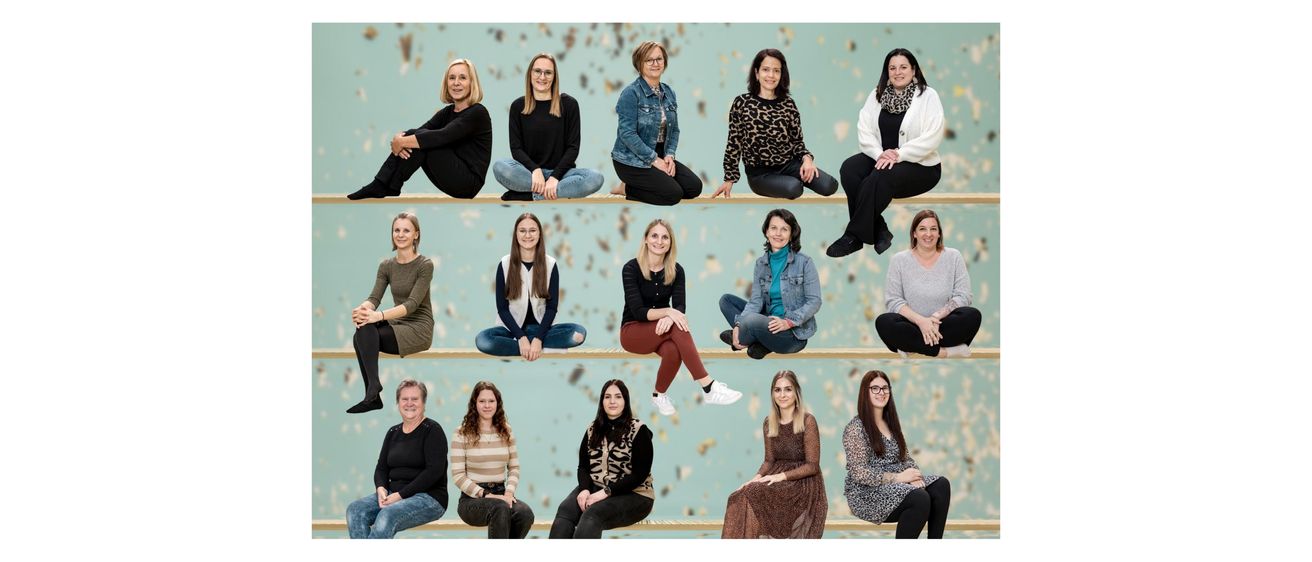 Eine Gruppe von Menschen sitzt auf einer Bank. Sie alle schauen in die Kamera. Sie tragen verschiedene Kleidungsstücke. Der Hintergrund ist unscharf.