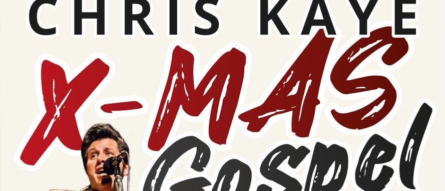 Ein Mann tritt auf der Bühne auf, spielt Gitarre und singt in ein Mikrofon vor einem Weihnachtsbaum.