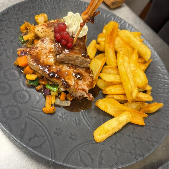 Ein Teller mit gegrilltem Hähnchen, garniert mit roten Beeren, Sahne und Gemüse, begleitet von goldenen Pommes frites.