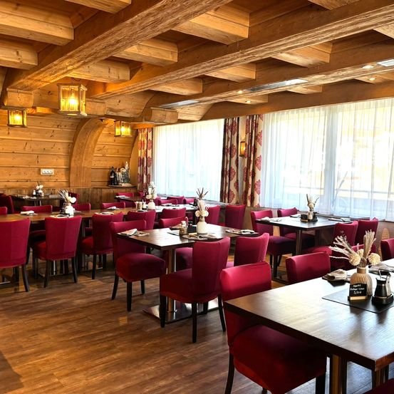Ein Restaurant mit Holzböden und -wänden, roten Stühlen und Tischen mit weißen Blumen und Tellern.