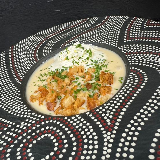 Eine cremige Suppe mit Croutons und Kräutern, serviert in einer dekorativen Schüssel mit schwarzem und weißem Muster.
