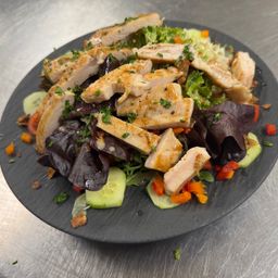 Ein Teller mit gegrilltem Hähnchensalat mit gemischten Salaten, Gurken und roten Paprikaschoten auf einem schwarzen Teller.