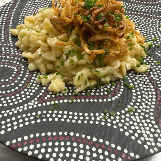 Ein Teller mit cremiger Pasta, überzogen mit knusprigen Zwiebelringen und grünen Schnittlauch. Der Teller hat ein schwarzes und weißes Punktemuster.