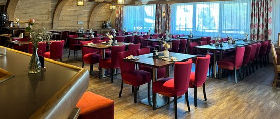 Ein Restaurant mit Holzböden und -balken, roten Stühlen und Tischen, die mit Blumen und Servietten gedeckt sind. Die Decke hat Lichter und ein dekoratives Design.