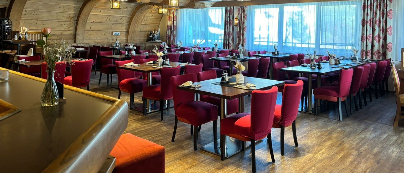 Ein Restaurant mit Holzböden und -balken, roten Stühlen und Tischen, die mit Blumen und Servietten gedeckt sind. Die Decke hat Lichter und ein dekoratives Design.
