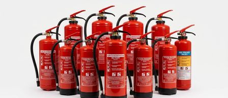 Eine Reihe roter Feuerlöscher mit schwarzen Düsen und silbernen Griffen steht in einer Reihe vor weißem Hintergrund.