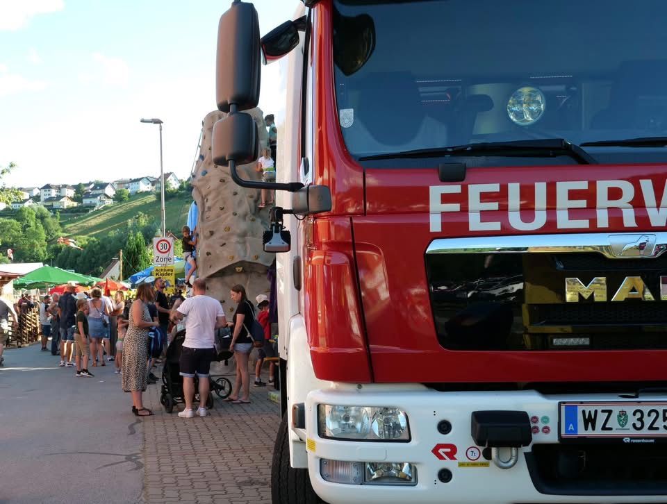 Ein Feuerwehrauto ist am Straßenrand geparkt, wo Menschen herumlaufen und einige auf einer Kletterwand klettern.