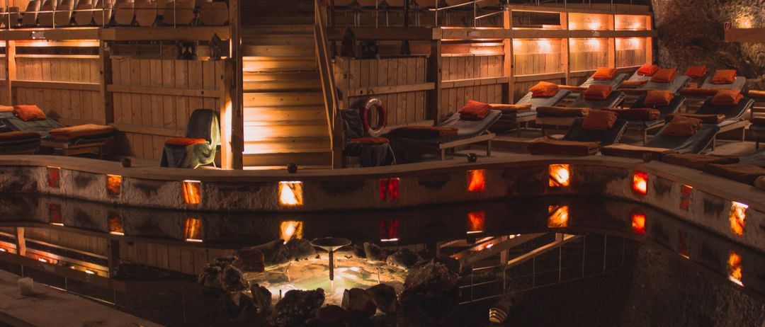 Ein kreisförmiger Innenpool mit einer Spa-ähnlichen Einrichtung, mit einer zentralen heißen Quelle und Liegestühlen am Rand, beleuchtet von warmen Lichtern.