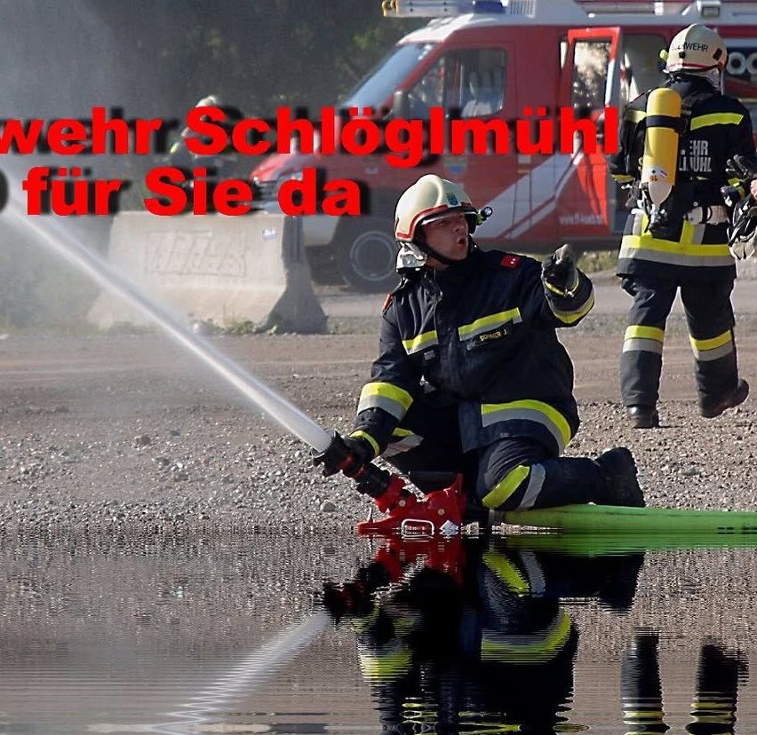 Feuerwehrleute sind bei einer Trainingsübung. Ein Feuerwehrmann sprüht Wasser, während ein anderer daneben steht. Der Text im Bild lautet Wehrwehr Schloglmuhl.