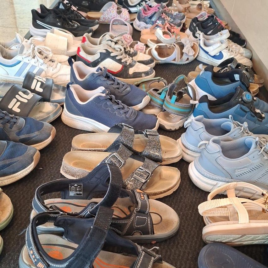 Eine Sammlung verschiedener Sneaker und Sandalen ist auf einer dunklen Oberfläche ausgestellt, darunter Marken wie Fila, Nike und Adidas.