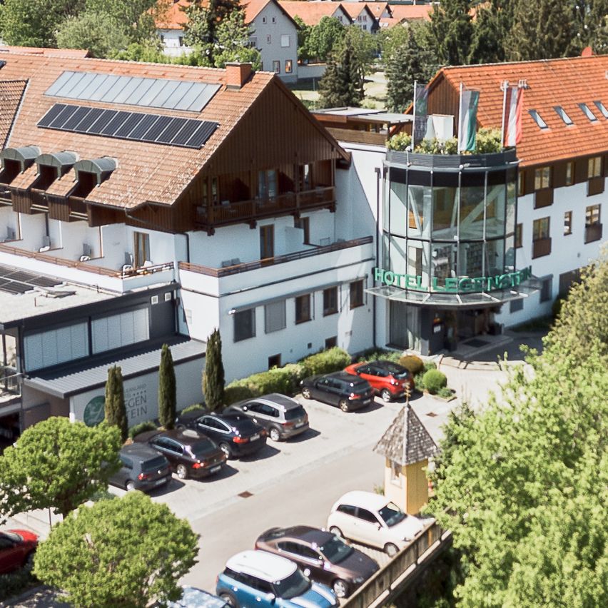 Eine Luftaufnahme eines Hotels mit Solarpanelen, umgeben von Bäumen, Häusern und Autos auf einem Parkplatz.