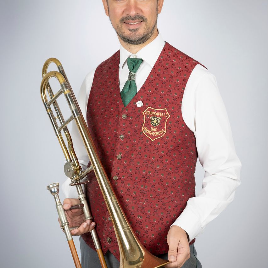 Ein Mann in einem roten Wams mit einem roten und grünen Logo darauf hält ein Posaune.