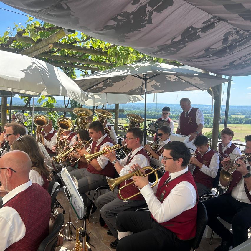 Ein Musikerensemble sitzt unter einem Baldachin und spielt Trompeten und andere Instrumente, mit einer malerischen Aussicht im Hintergrund.