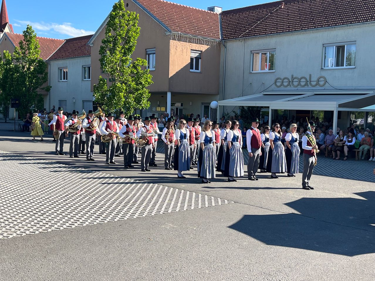 A marching band performs in front of a building with the sign 'CABALA' on a sunny day.