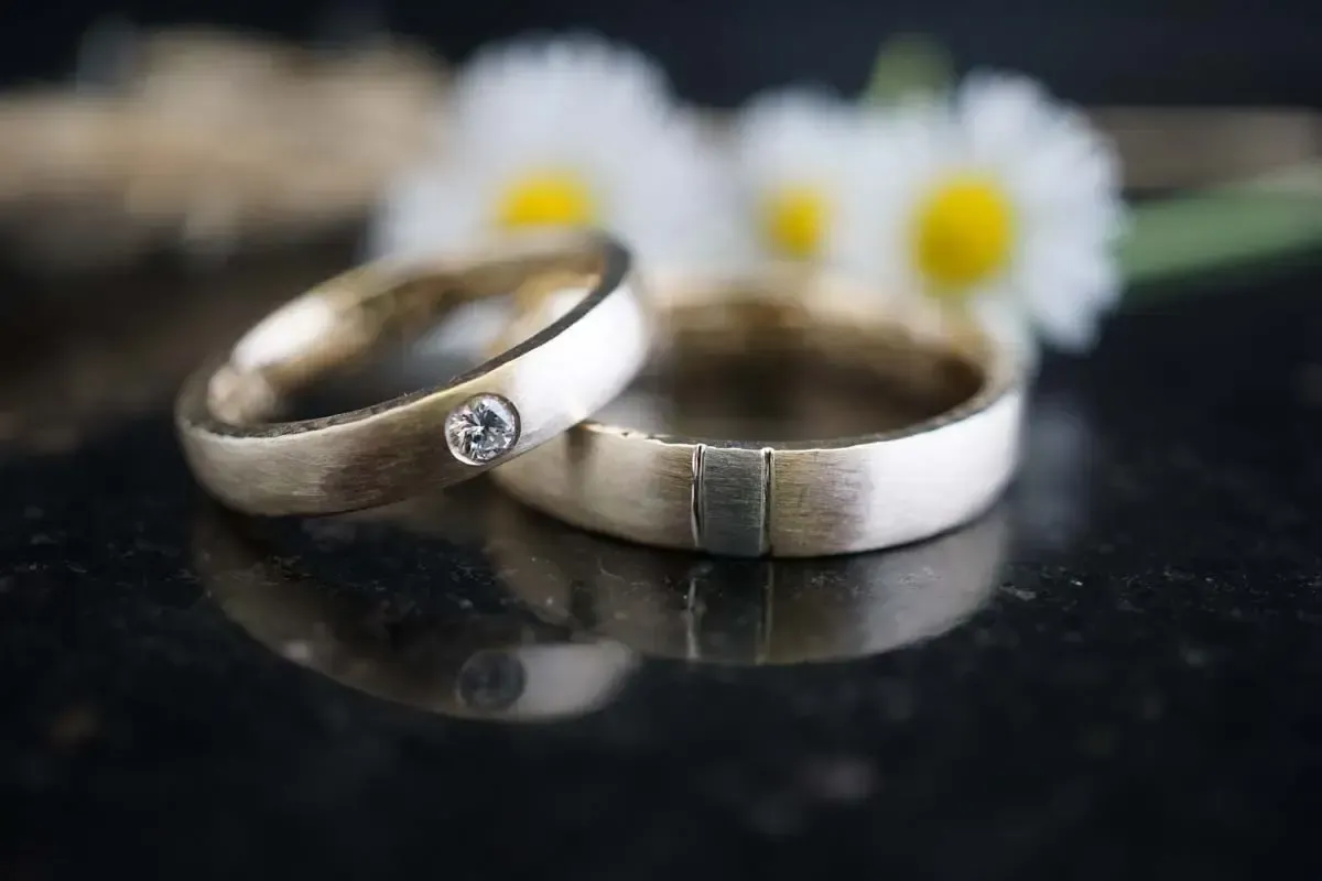Zwei Silberringe mit einem Diamanten auf einem, auf einer schwarzen Oberfläche mit verschwommenen Gänseblümchen im Hintergrund.