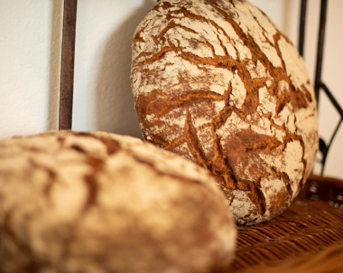Two round loaves of bread are placed on a wicker basket. One loaf has visible scoring on its crust, while the other loaf has a more uniform appearance.
