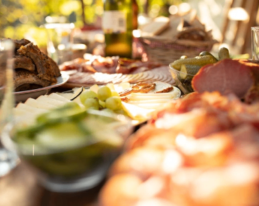 A table is set with a variety of meats, cheeses, and vegetables. There are sliced ham, sausages, and other dishes. A bottle of wine is also present.