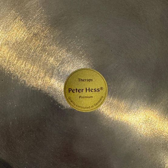 Ein Nahaufnahme einer glänzenden metallischen Oberfläche zeigt einen runden gelben Aufkleber mit der Aufschrift 'Therapie Peter Hess Premium Qualität kontrolliert in Deutschland.'
