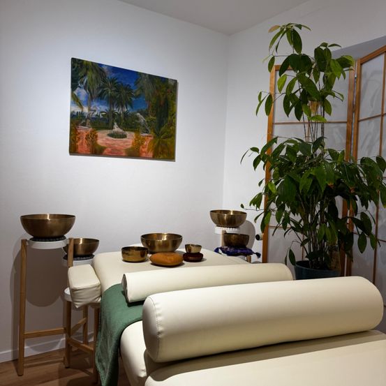 Ein Spa-Raum mit weißer Wand, Gemälde, Pflanze und zwei Massagetischen mit Schalen und Kissen.