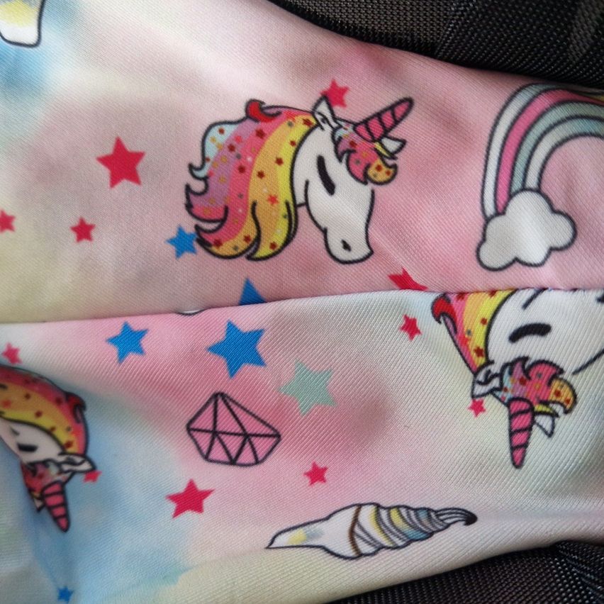 Ein Nahaufnahme eines rosa Stoffs mit einem Einhorn, einem Regenbogen und Sternen. Darunter sind ein Eisbecher, ein Diamant und ein weiteres Einhorn abgebildet.