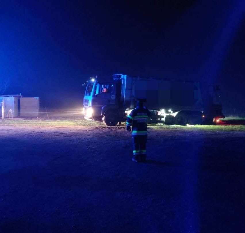 Ein Feuerwehrmann steht bei Nacht vor einem Lastwagen, der von blauen Lichtern beleuchtet wird. Der Lastwagen ist auf der Straße geparkt.
