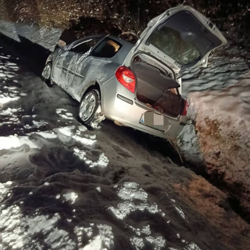 Ein silbernes Auto mit offenem Kofferraum steckt im Schnee fest, geneigt zur Seite mit dem vorderen Ende tiefer als hinten.