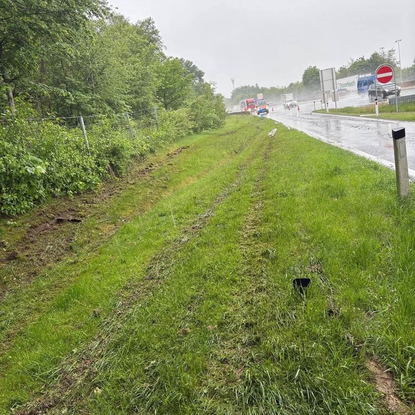 A highway with vehicles driving in heavy rain. There are tire marks on the grassy area beside the road. A red and white signboard is visible on the right side.