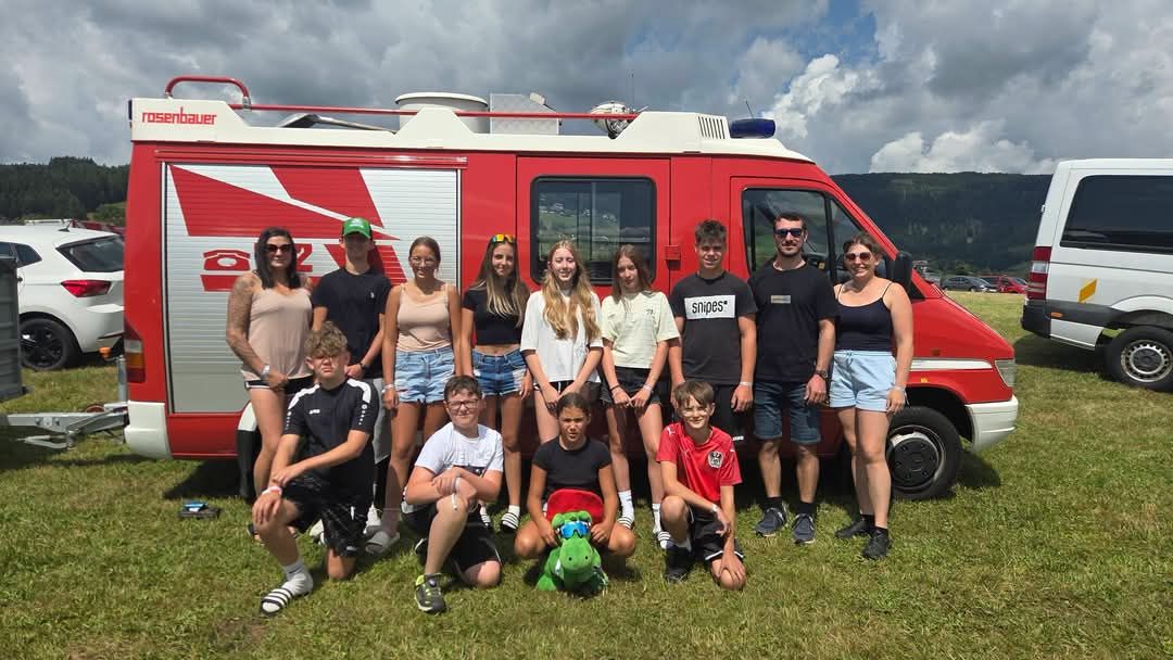 Jugendfeuerwehr-Mitglieder posieren vor einem roten Feuerwehrfahrzeug in Österreich.