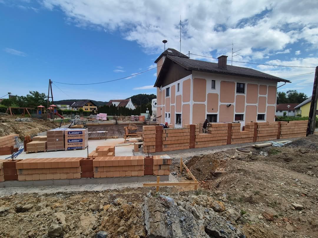 Bauarbeiten in Österreich: Ziegelmauer wird errichtet, Hausfassade und Spielplatz im Hintergrund