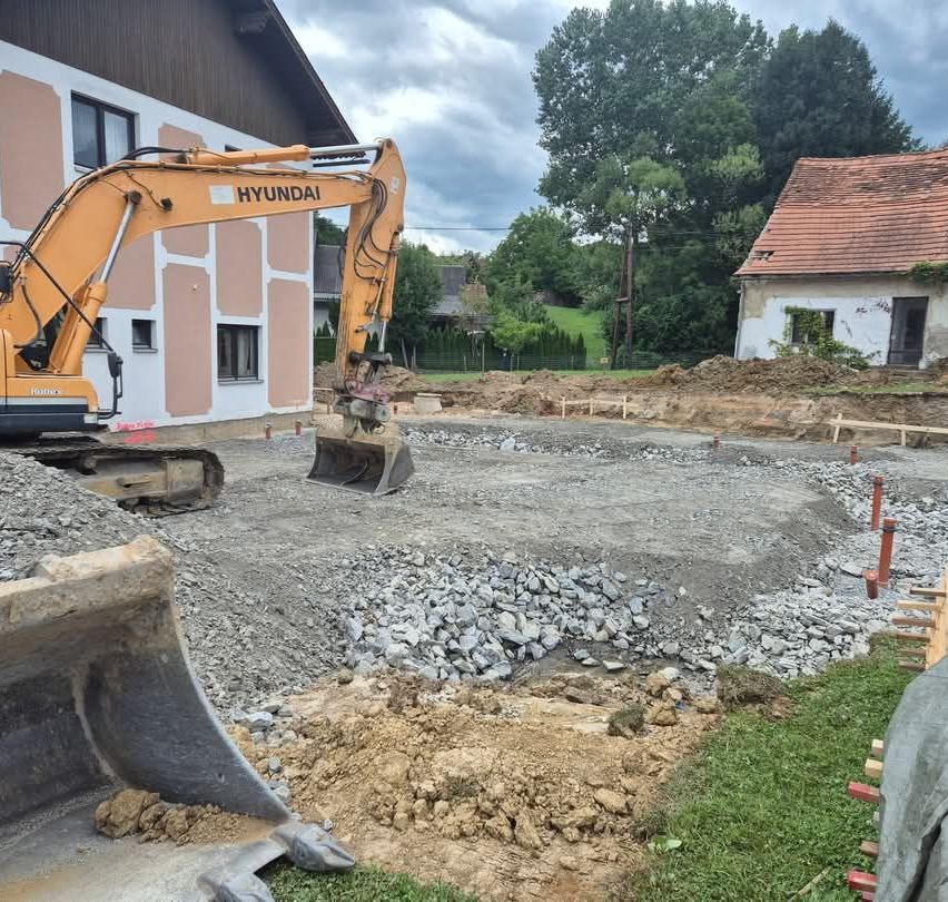 Ein Hyundai-Bagger gräbt ein Loch auf einer Baustelle mit einem Haus im Hintergrund.